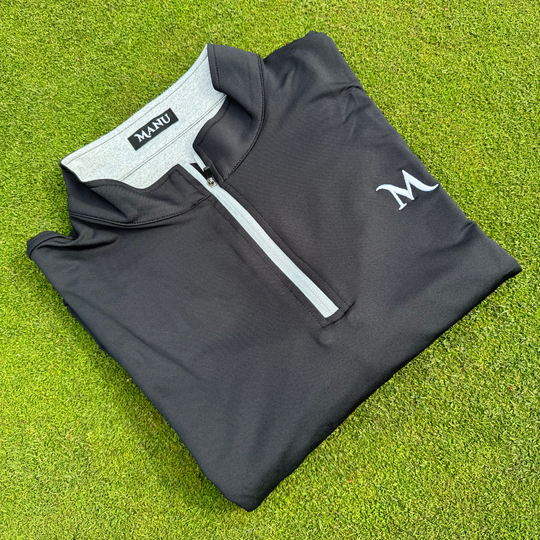 1/4 zip pullover in black laid on green grass, stylish and perfect for golf, showcasing moisture-wicking fabric.