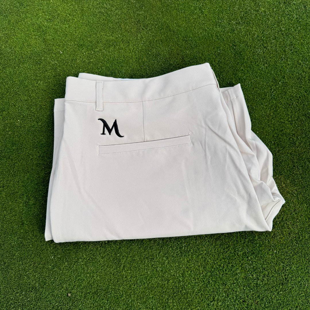 Cream Manu Shorts folded on green turf, highlighting lightweight and stylish golf shorts for men.