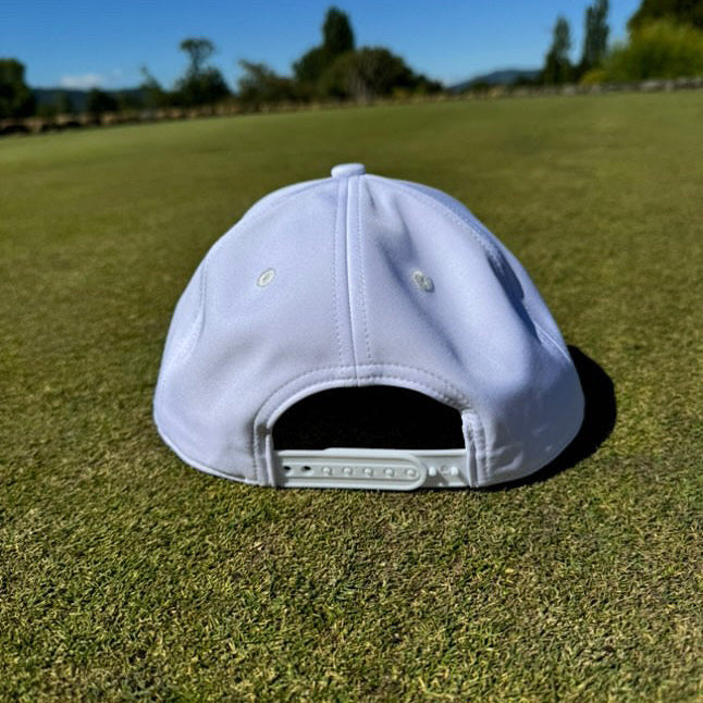 Back view of a stylish white Manu Golf Hat on green golf course grass.